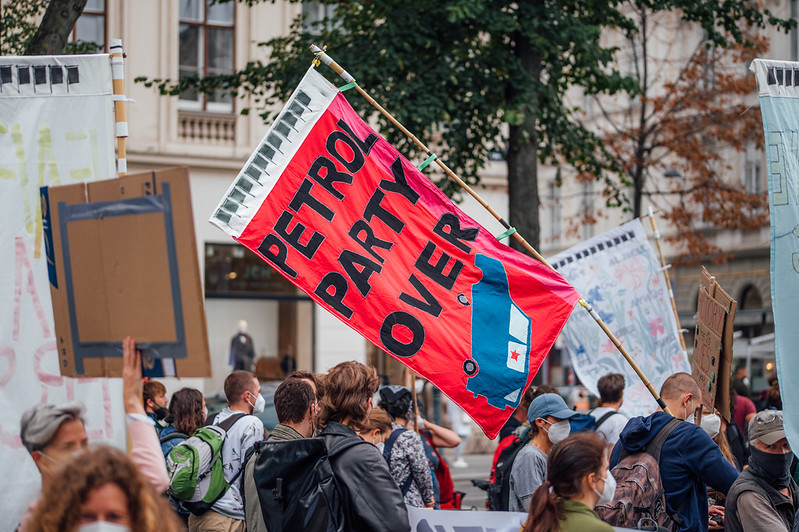 Protester holding a flag with a car on its roof and the message 